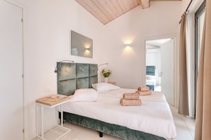 A modern bedroom with a large bed, a bedside table, a mirror, and a view of the bathroom.