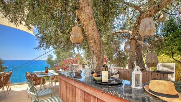 An outdoor bar area with a view of the sea, wooden furniture, and hanging lanterns.