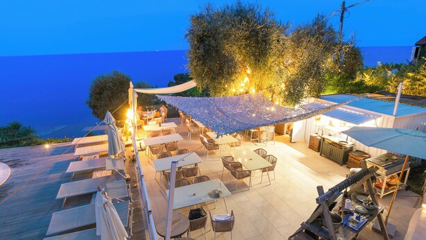 Ein Außenbereich mit Terrasse, Tischen, Stühlen, einer Bar und Meerblick.