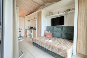 Ein modernes Schlafzimmer mit Schlafsofa, Flachbildfernseher und einer Küchenzeile im Hintergrund.
