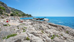 A rocky beach with clear blue water, a stone wall, and a few people.