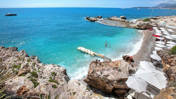 A coastal beach with rocky terrain, a pier, and beach umbrellas. - Boutique Pool Apt. Balzi Rossi - Roma 5, Ventimiglia, Italy (Ventimiglia)