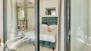 A modern bedroom with a glass door leading to a balcony, a bed with a green headboard, and a small mirror on the wall. - Boutique Pool Apt. Balzi Rossi - Roma 4, Ventimiglia, Italy (Ventimiglia)