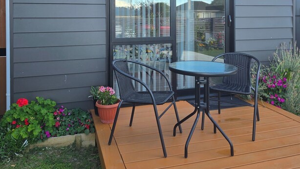 Eine moderne Terrasse mit Holzdeck, einer Glastür und einem Tisch mit Stühlen.
