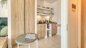 Una cocina compacta con armarios blancos, una pequeña encimera y un comedor con una mesa redonda.