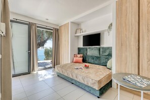 Un dormitorio con cama, televisor, una mesita y un ventanal corredera que da a un área exterior.