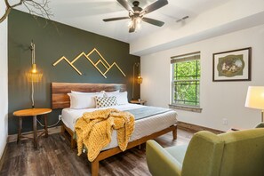 Un dormitorio con cama, piso de madera, ventilador de techo, ventana con vistas e iluminación empotrada.