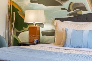 A bed with a quilted cover, a bedside lamp, and a wall with a camouflage pattern.