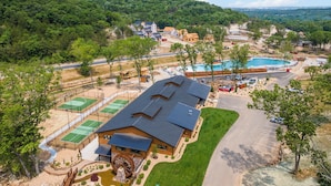 A residential area with multiple houses, a swimming pool, tennis courts, and a large wooden wheel structure.