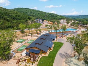 A residential area with multiple houses, a swimming pool, tennis courts, and a large wooden wheel structure.