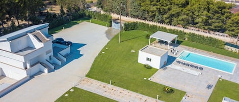 An aerial view of a modern residential property with a swimming pool, a covered patio, and a well-maintained lawn.