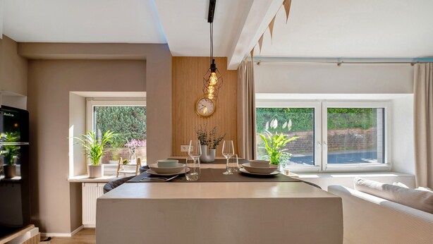 A modern kitchen with a central island, a dining area with a sofa, and large windows with a view of greenery. - Holiday Apartment 'My Little Suite' with Wi-Fi (Illingen)