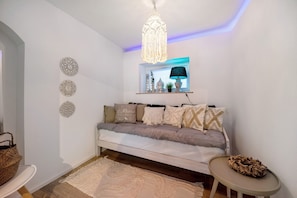 Un salon chaleureux avec un canapé blanc, des œuvres d’art décoratives accrochées au mur, un luminaire suspendu et une petite table sur laquelle repose un panier en osier.