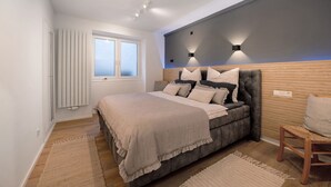 A bedroom with a bed, a chair, a window, and a wall-mounted light fixture. - Holiday Apartment 'My Little Suite' with Wi-Fi (Illingen)