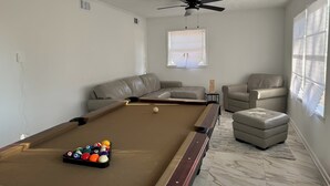 A pool table with balls, a ceiling fan, a window with blinds, a sofa, and a chair. - Charming 3-bedroom house in Atlanta with AC, WiFi (Atlanta)