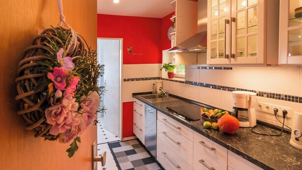 A kitchen with white cabinets, a black countertop, and a red accent wall.