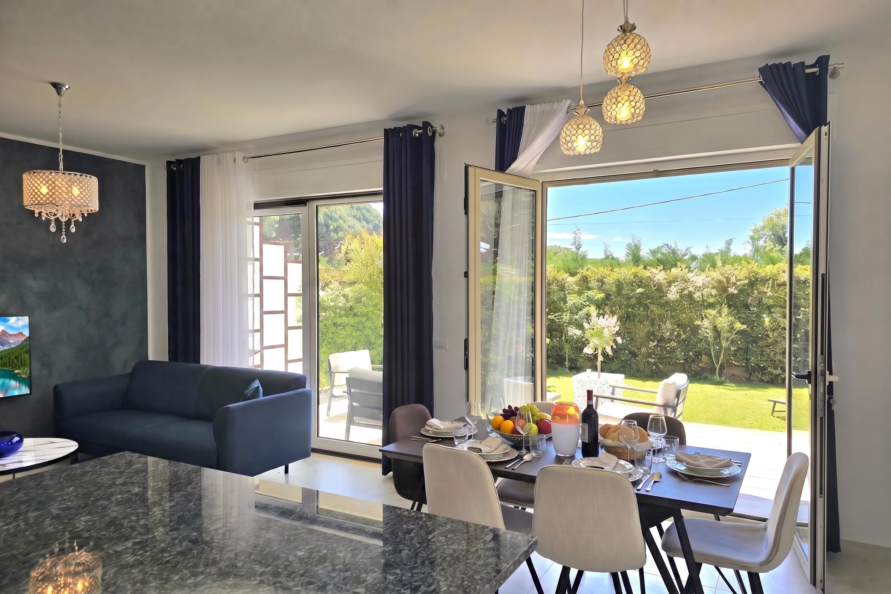 A modern dining area with a marble table, chairs, and a view of a garden through glass doors.