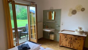 A room with two beds, a bathroom with a sink and mirror, and a view of a garden through a sliding door. - Holiday Home 'Durst 1' with Mountain Views, Private Terrace and Wi-Fi (Mayrhofen)