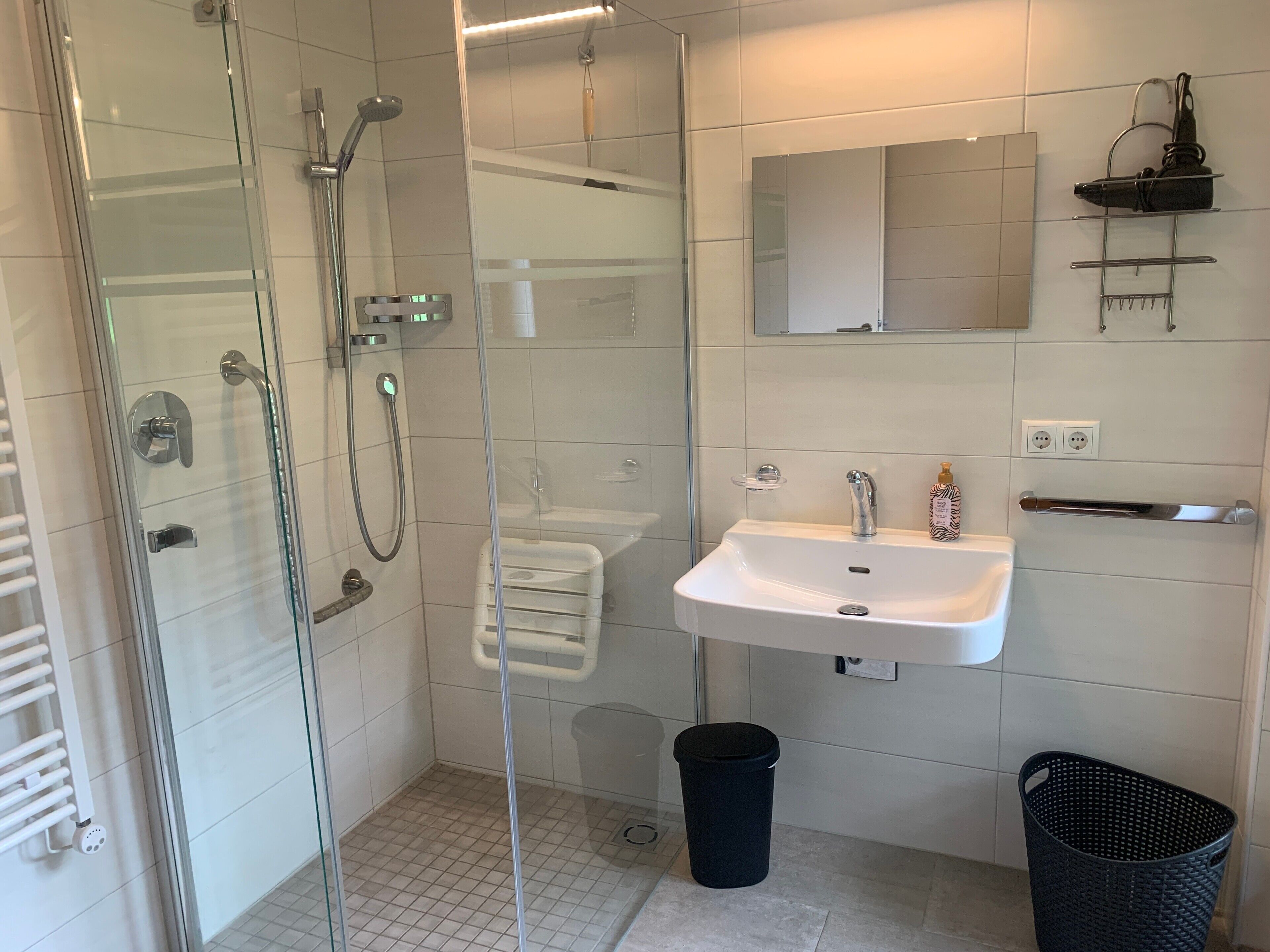 A modern bathroom with a glass-enclosed shower, a white sink, and a black trash bin.