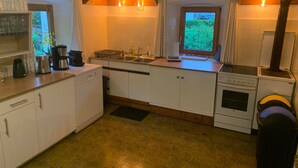 Une cuisine de taille réduite, avec des meubles blancs, un évier, une cuisinière et une fenêtre agrémentée de rideaux.