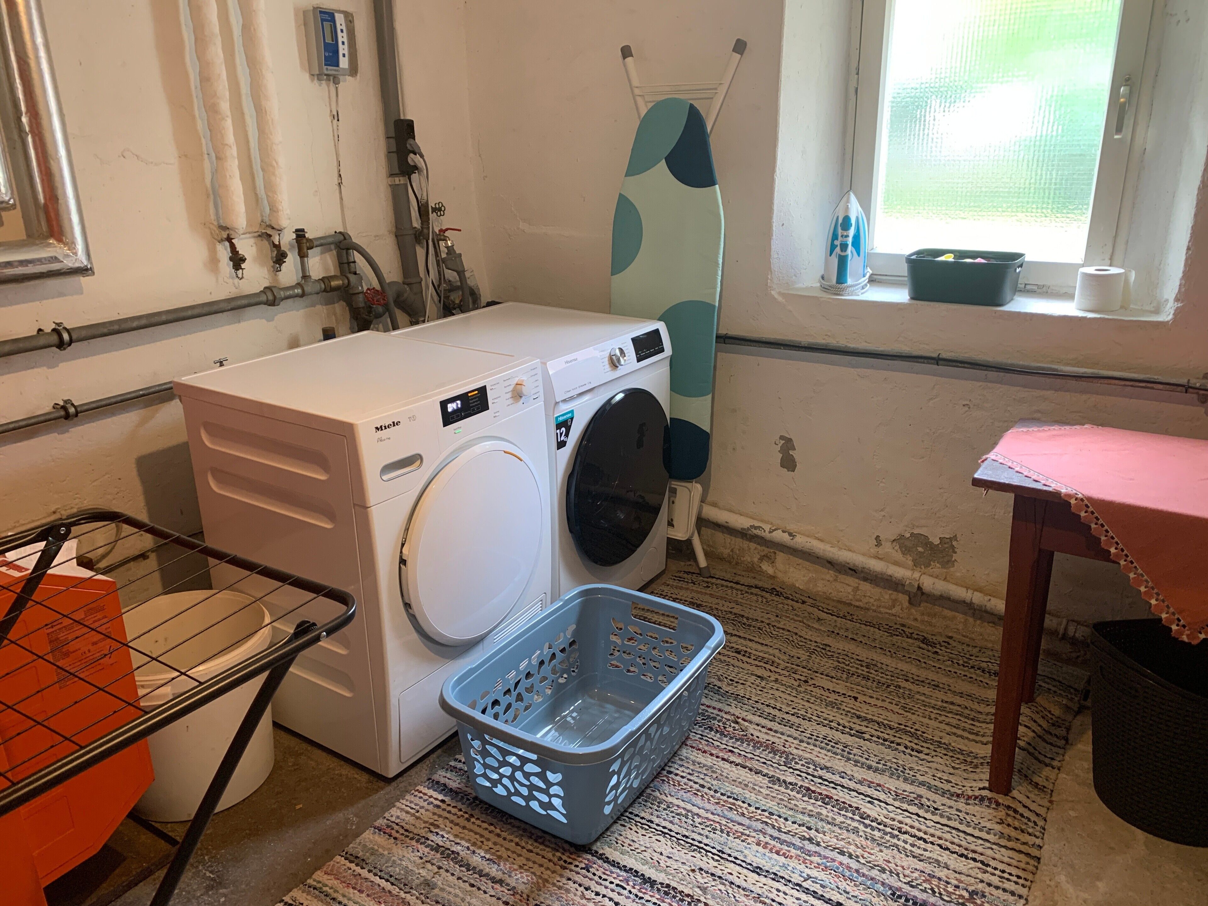 Een wasserette met een voorlader wasmachine, een droger, een droogrek en een raam met uitzicht.