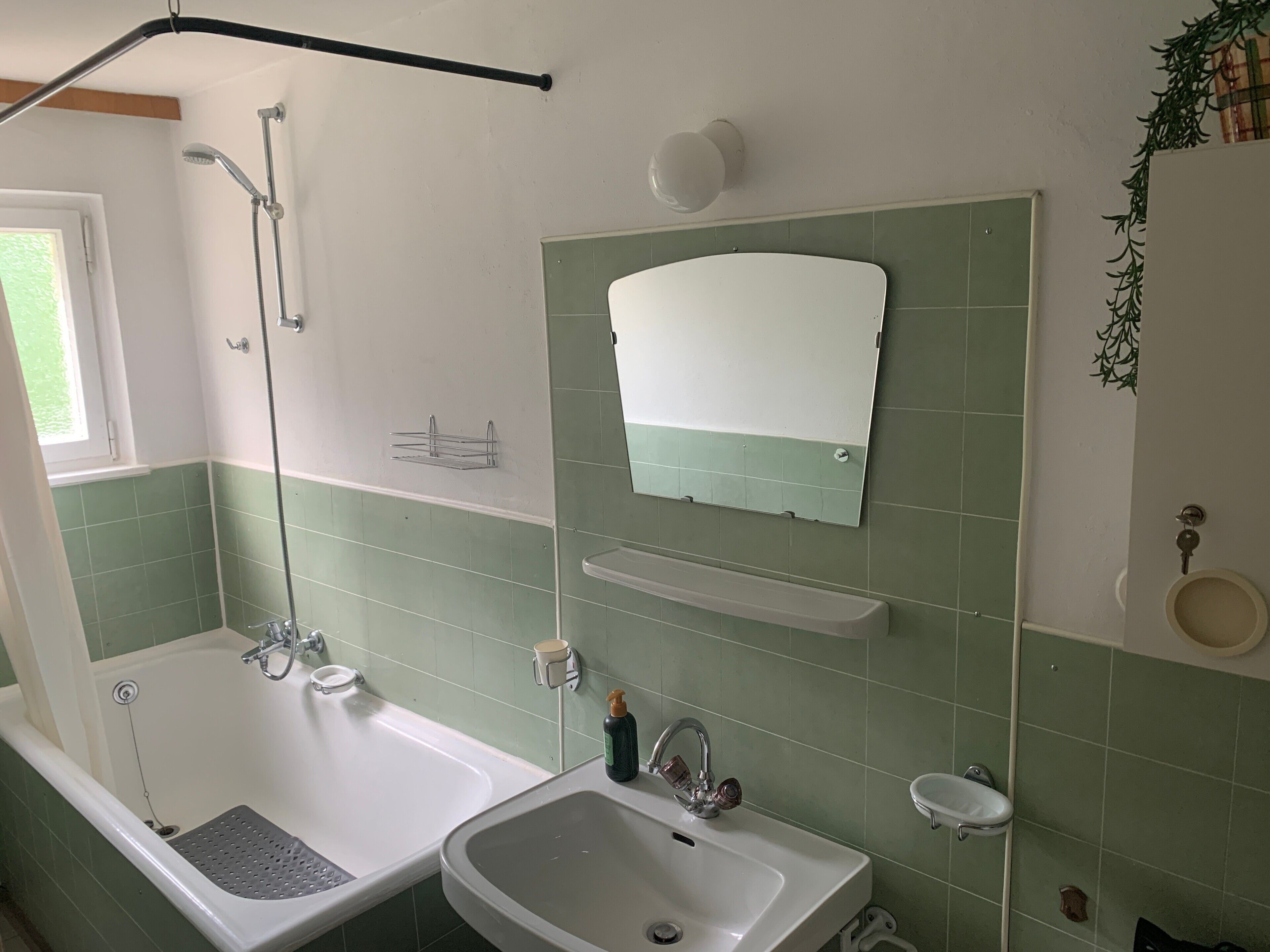 A bathroom with a bathtub, sink, mirror, and green-tiled walls.