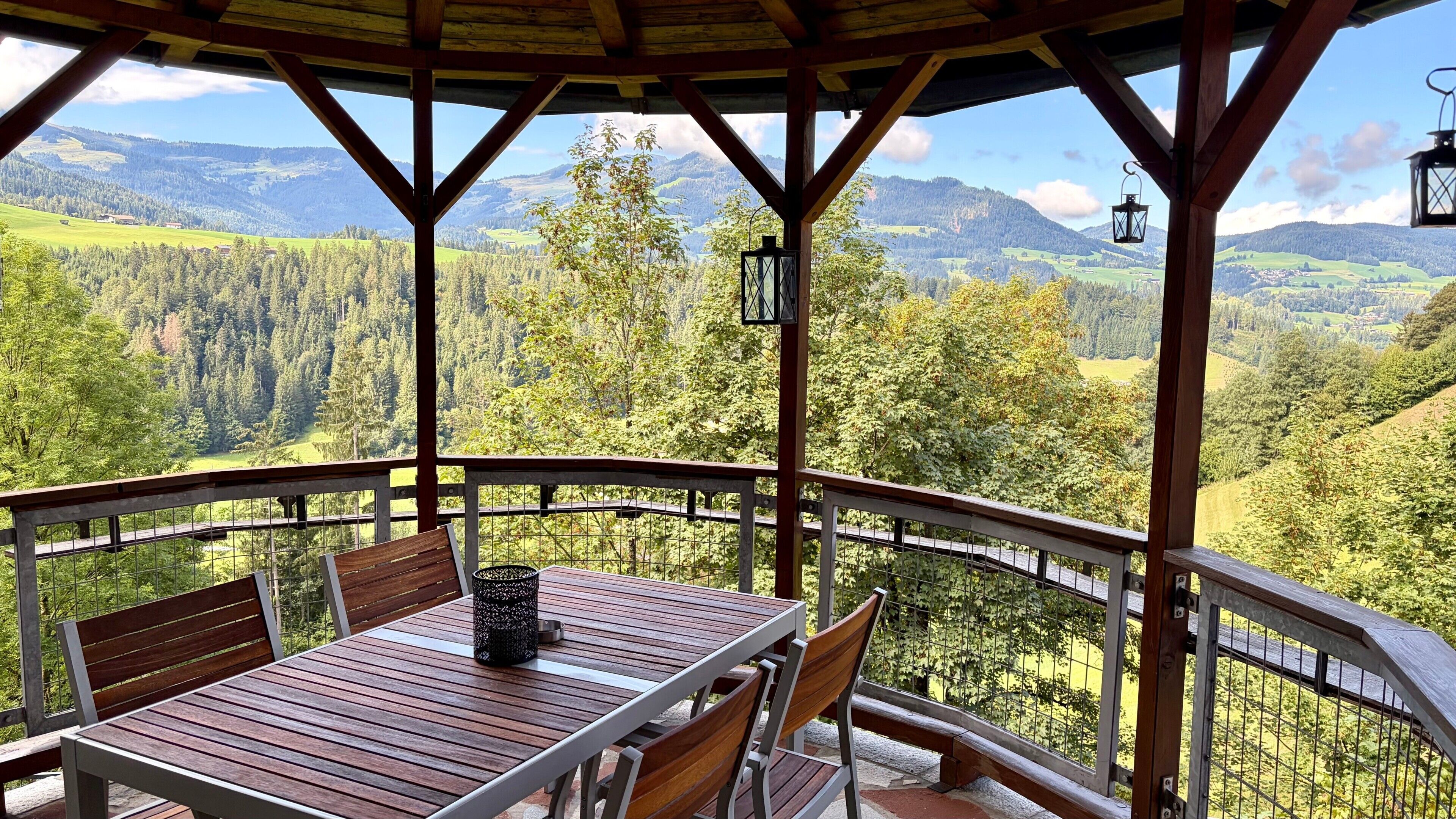 A wooden deck with a table and chairs, overlooking a mountainous landscape.