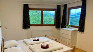 A bedroom with a wooden bed, white bedding, a radiator, a window with curtains, and a small plant on a dresser.