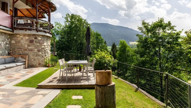 A stone building with a wooden deck, outdoor seating, and a view of mountains.