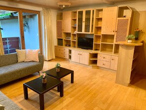 A living room with a sofa, two coffee tables, wooden cabinets, a TV, and a window with curtains. - Apartment 'Auner Top 1' with Mountain View, Private Terrace and Wi-Fi (Westendorf)