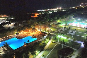 A nighttime view of a resort with a swimming pool, landscaped gardens, and a tennis court. - Perla Holiday Villa 150, Lalzit Bay, Albania (Lalzit Bay)