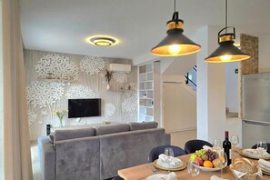A modern living room with a grey sofa, a dining table set with plates, glasses, and a fruit bowl. - Perla Holiday Villa 150, Lalzit Bay, Albania (Lalzit Bay)