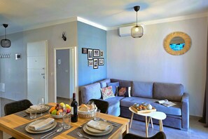 A modern living room with a grey sofa, a dining table set for two, and a small side table with a tray of food and drinks.
