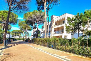 Un camino pavimentado bordeado de árboles y un edificio moderno con balcones.