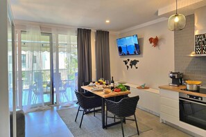 A modern kitchen with a dining area, a TV mounted on the wall, and a balcony with outdoor furniture.
