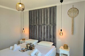 Un dormitorio moderno con cabecera capitonada, cama con ropa de cama blanca, dos mesitas de noche y decoración mural.
