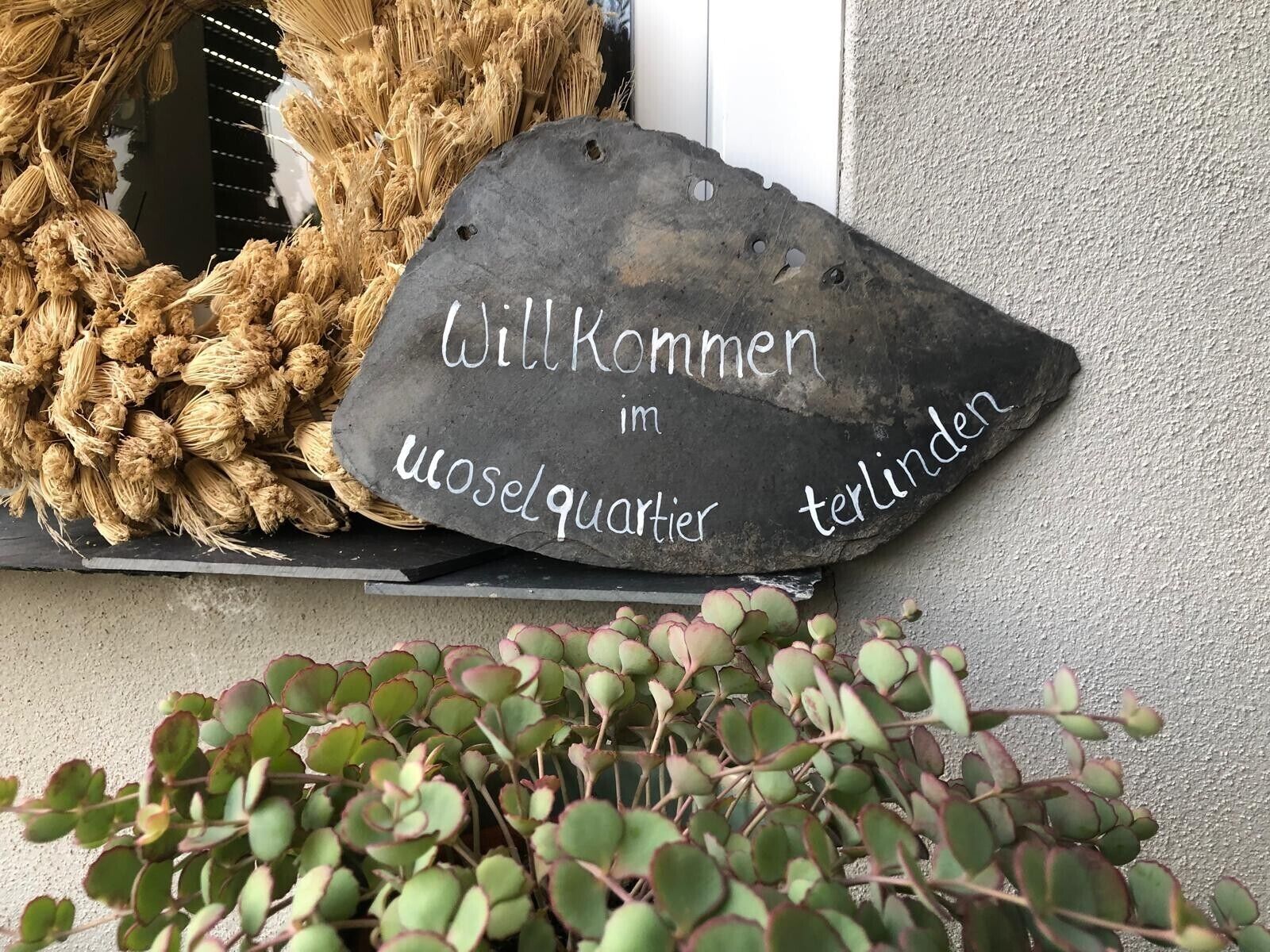 A welcome sign with text, a woven wreath, and a potted plant.