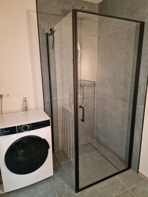 Un baño moderno con cabina de ducha de vidrio, lavadora integrada y suelo de baldosas.