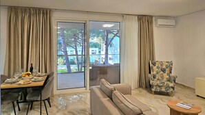 Una sala de estar con un sofá, un comedor, un sillón estampado y un ventanal corredero que da a un espacio exterior.