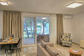 A living room with a sofa, a dining table set, a patterned armchair, and a sliding glass door leading to an outdoor area.