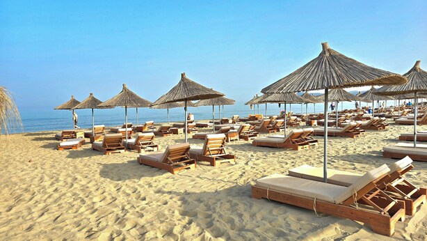 Una playa con sillones de madera y sombrillas de paja.
