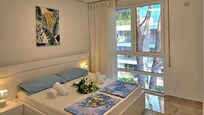 Habitación de hotel con cama, ventana con cortinas, una obra de arte colgada en la pared y vistas a árboles y edificios.