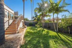 A backyard with a wooden staircase leading to a deck, surrounded by palm trees and a wooden fence. - Coastal 2BR w/ Large Private Yard & Deck – Walk to Beach & Dining (Solana Beach)