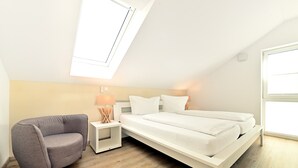 A bedroom with a bed, a gray sofa, a nightstand with a lamp, and a skylight. - Apartment 'Dinkelbach Traumblick 3 B' with Lake View, Balcony and Wi-Fi (Wasserburg (Bodensee))