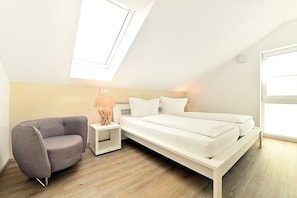 Une chambre à coucher avec un lit, un canapé gris, une table de chevet avec une lampe et une lucarne.