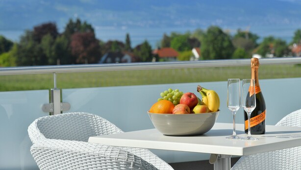 A table with a fruit bowl, two glasses, and a bottle of champagne. - Apartment 'Dinkelbach Traumblick 3 B' with Lake View, Balcony and Wi-Fi (Wasserburg (Bodensee))