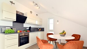A modern kitchen with white cabinets, a black oven, and orange chairs around a white table. - Apartment 'Dinkelbach Traumblick 3 B' with Lake View, Balcony and Wi-Fi (Wasserburg (Bodensee))