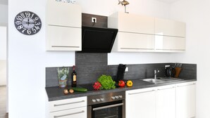 A modern kitchen with white cabinets, a black range hood, a built-in oven, a sink, and a clock on the wall. - Apartment 'Dinkelbach Traumblick 3 B' with Lake View, Balcony and Wi-Fi (Wasserburg (Bodensee))