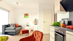 A modern living room with a sofa, ottoman, and a dining table with fruit. - Apartment 'Dinkelbach Traumblick 3 B' with Lake View, Balcony and Wi-Fi (Wasserburg (Bodensee))