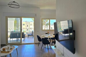 A dining area with a table set for six, a TV mounted on the wall, and a sliding glass door leading to an outdoor seating area.